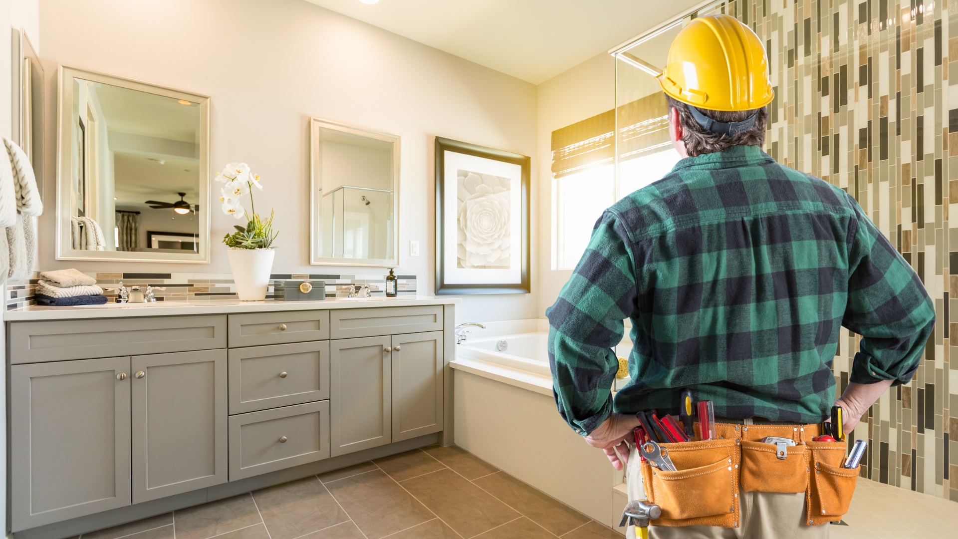 A contractor assessing a newly remodeled bathroom with gray cabinets and a stylish tile backsplash