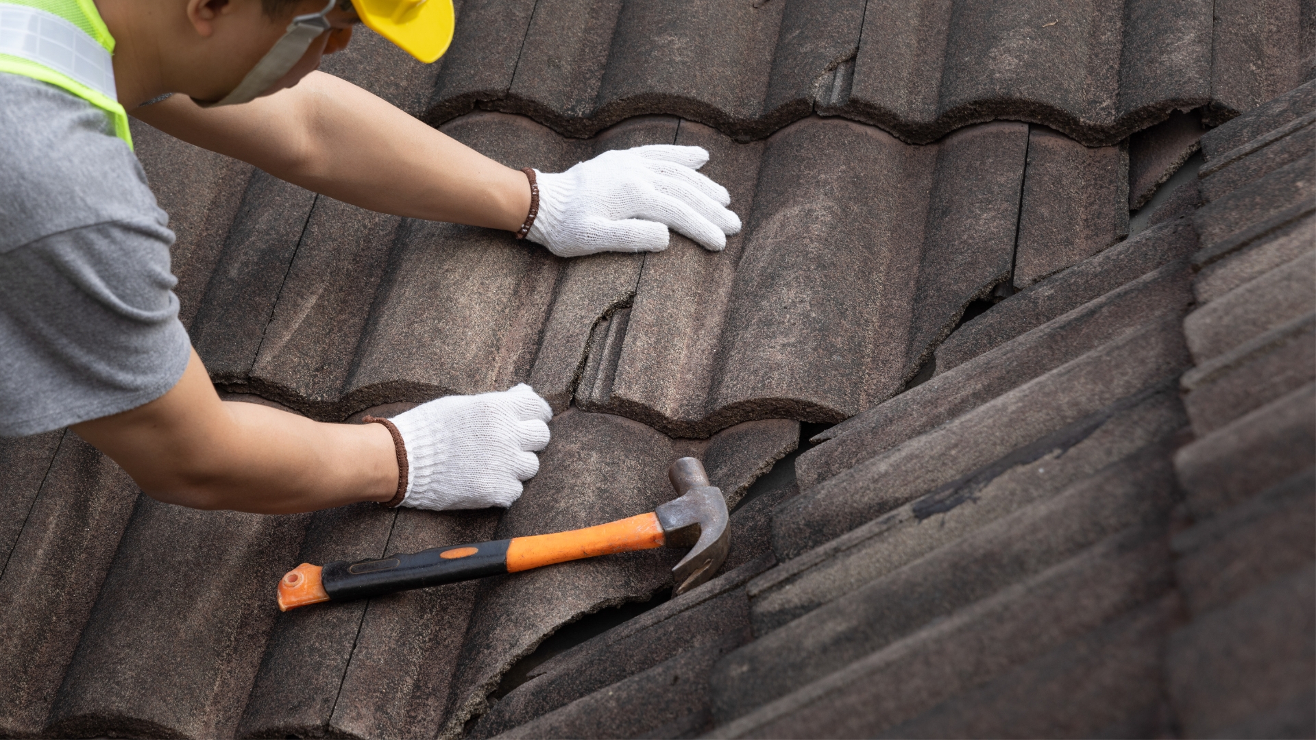 Roof repair in progress as worker replaces cracked tiles on residential roof.